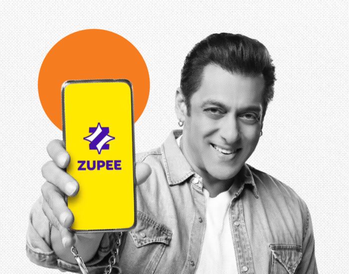 Actor Salman Khan smiling and holding up a smartphone that displays the yellow and purple Zupee app logo.